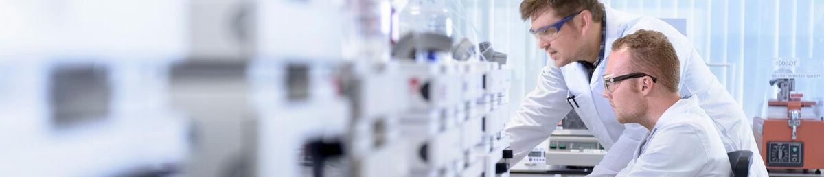 Side angle view of two scientists in a lab at a desk, analysing what’s in front of them